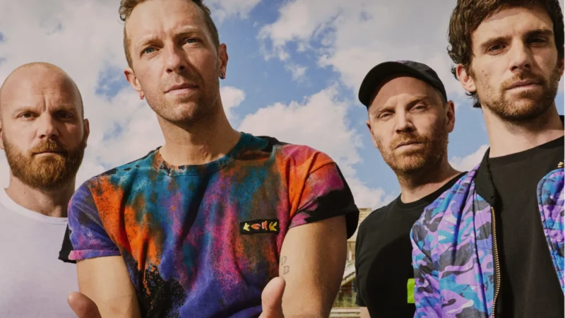 Imagem dos integrantes da banda Coldplay durante apresentação ao vivo com luzes coloridas