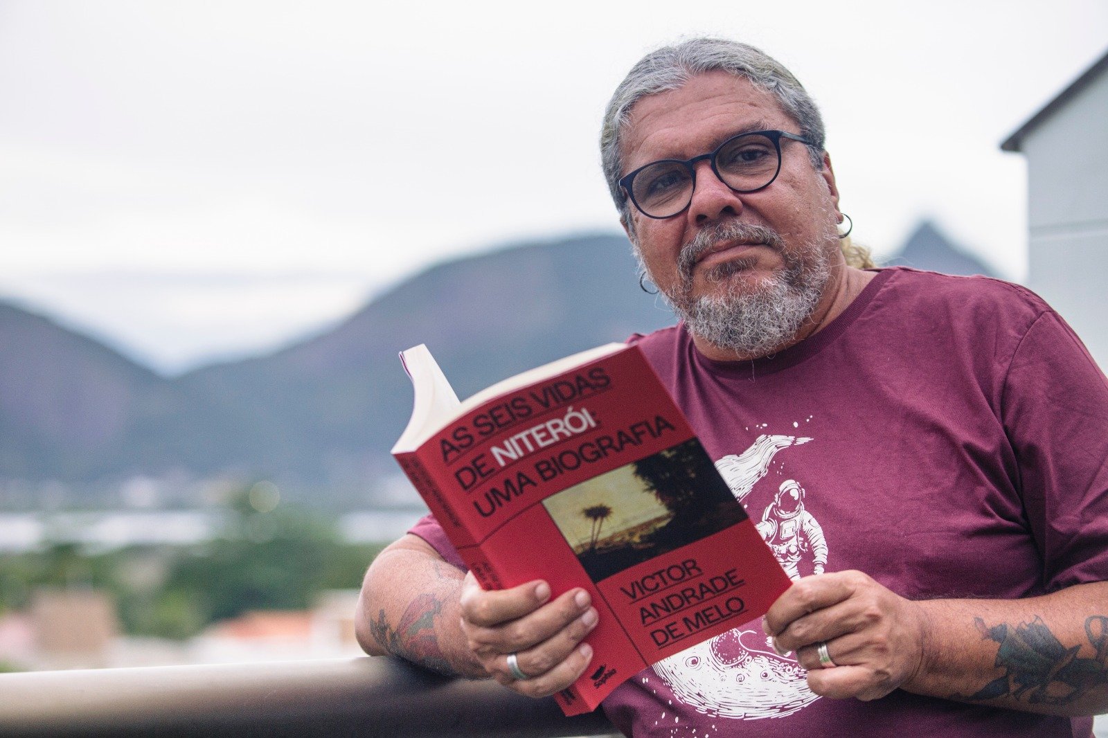 Foto de Victor Andrade segurando o livro ‘As seis vidas de Niterói’, Biografia em lançamento na UFF e na Livraria Folha Seca