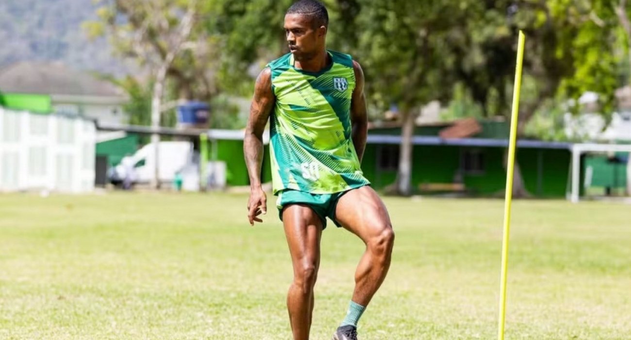 Douglas Costa em treino no Boavista buscando novo clube Douglas Costa, jogador de futebol, em treinamento individual com bola no gramado do Boavista, vestindo uniforme verde e preto, com cone de treinamento ao lado. Ele foca em manter a forma física enquanto busca um novo clube.