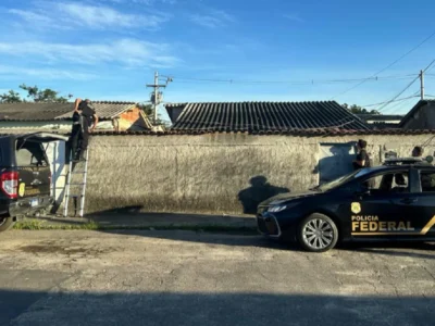 Policiais federais sobem escada e inspecionam o telhado de residência durante operação contra fraude.