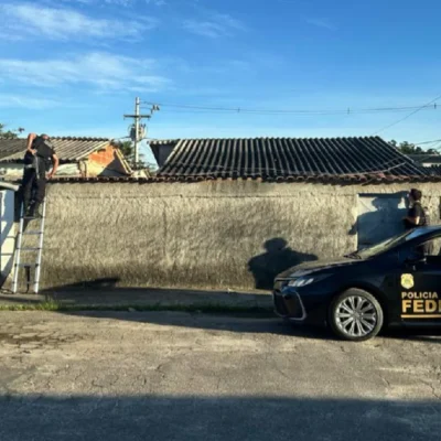 Policiais federais sobem escada e inspecionam o telhado de residência durante operação contra fraude.