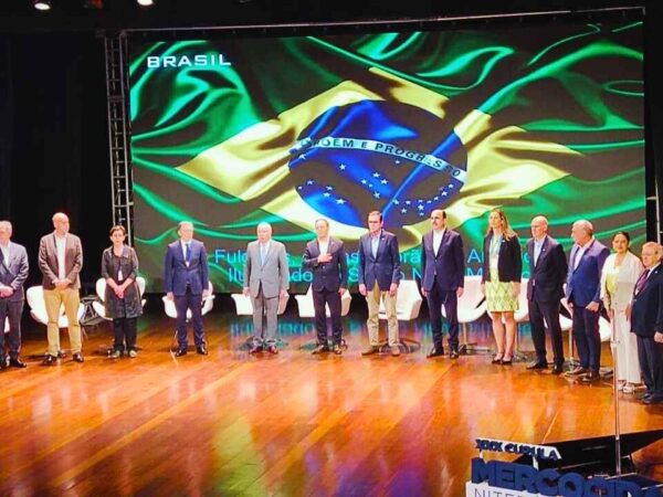Dezesseis autoridades brasileiras e internacionais, alinhadas sobre o palco do Teatro Municipal de Niterói, diante de um grande painel com a bandeira do Brasil iluminada, participam da XXX Cúpula do Mercocidades. À direita, um apresentador faz locução no púlpito.” Na ocasião, houve o anúncio de que a cidade do Rio de Janeiro terá escola para formação de líderes na Segurança Pública.