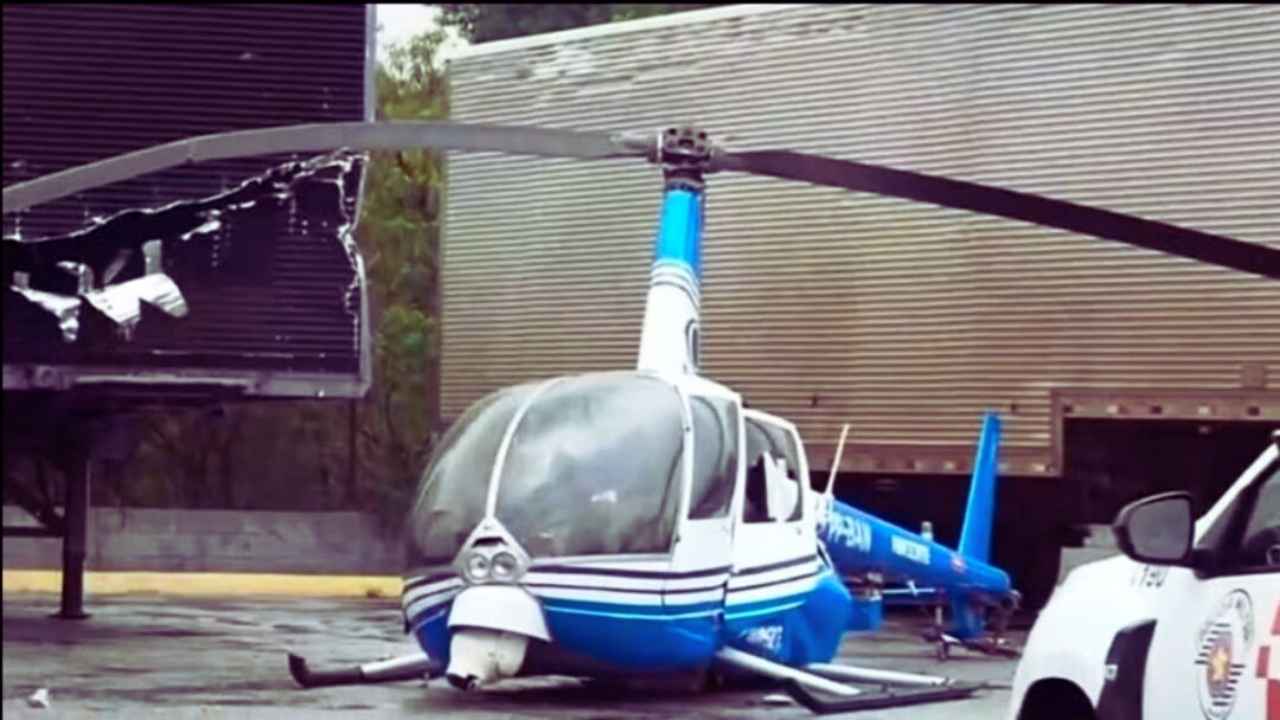 Helicóptero da Band, modelo Robinson R44 azul e branco, com danos na estrutura após pouso forçado em pátio de transportadora, em caso que nos remete à morte de Ricardo Boechat