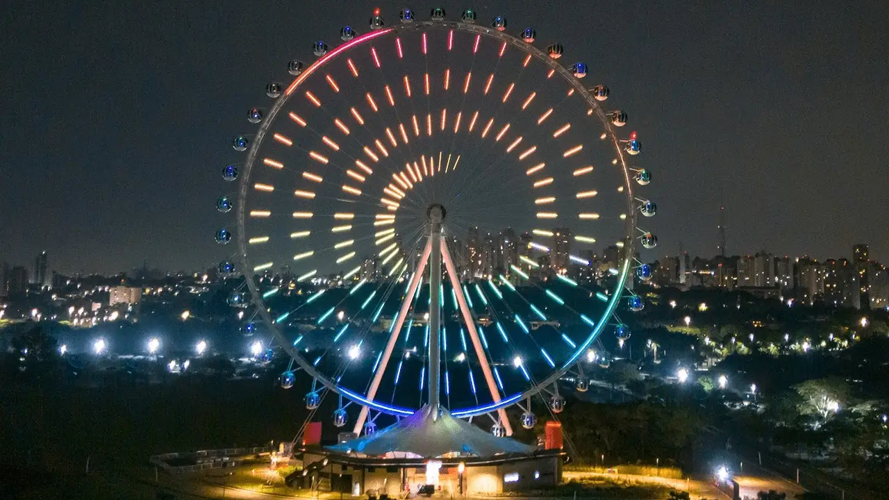 Roda gigante Roda Rico em São Paulo iluminada com um padrão espiral de luzes LED coloridas à noite, com o skyline da cidade ao fundo.