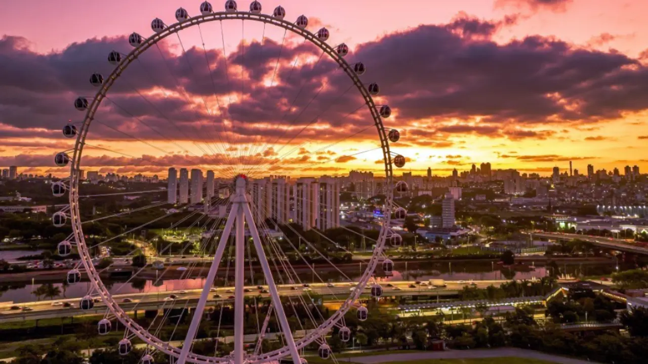 A Roda Gigante Rico no Parque Cândido Portinari durante um pôr do sol dramático com nuvens alaranjadas sobre a cidade de São Paulo.