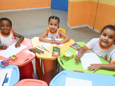 Alunos novos realizando atividades escolares em mesas coloridas, representando o ingresso em novas vagas da educação pública de Niterói.