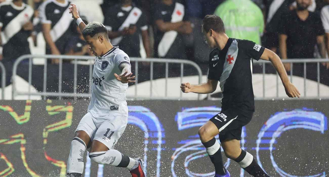 Disputa de bola entre jogadores do Vasco e Botafogo sob forte chuva em São Januário