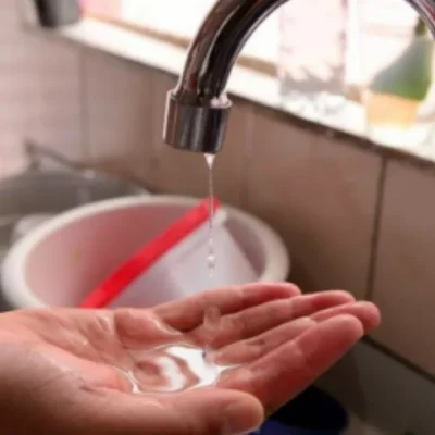 Gota de água pendurada em torneira metálica, representando risco de interrupção no abastecimento.