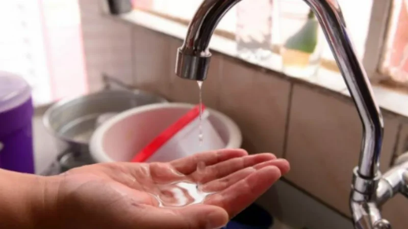 Gota de água pendurada em torneira metálica, representando risco de interrupção no abastecimento.