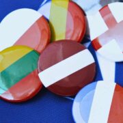 Vários bótons circulares estampados com bandeiras de diferentes países, incluindo França e Inglaterra, agrupados sobre um tecido azul-escuro com linhas brancas de fundo.