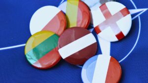 Vários bótons circulares estampados com bandeiras de diferentes países, incluindo França e Inglaterra, agrupados sobre um tecido azul-escuro com linhas brancas de fundo.