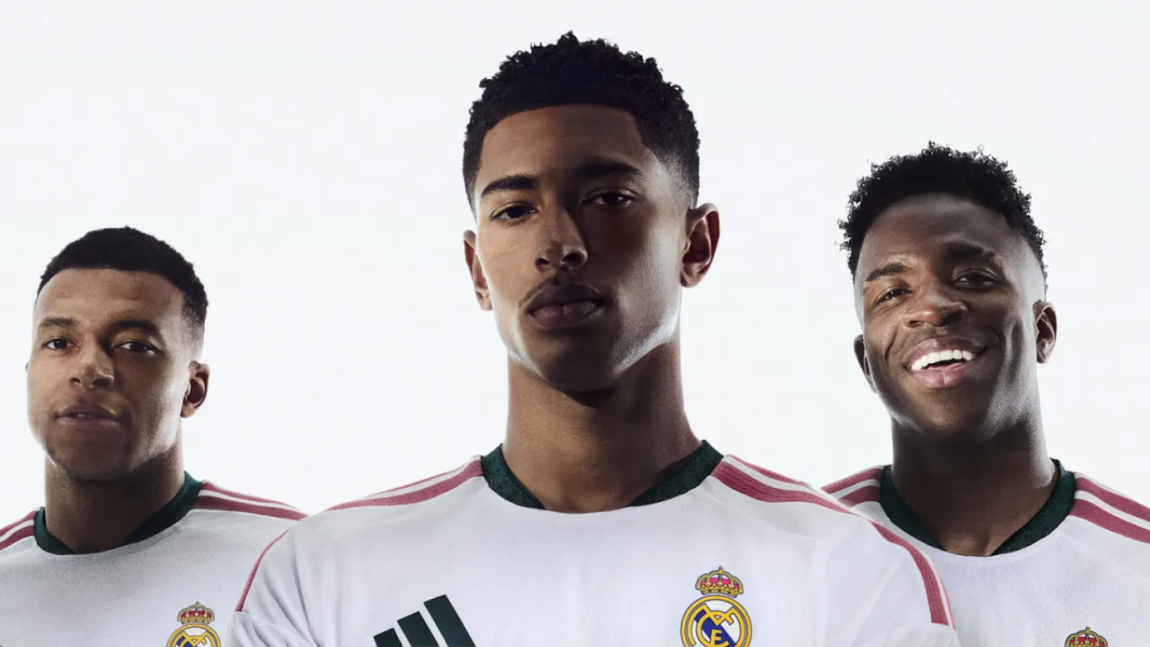 Vini Jr, Mbappé e Bellingham usando a camisa branca do Real Madrid 2026/27 com detalhes rosa e verde