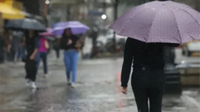 Pessoas caminham sob chuva durante período de tempo instável