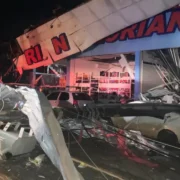 Imagem da passagem do ciclone provocou danos em lojas e carros parados na rua, com diversos destroços na rua e um poste caído em cima de um carro branco