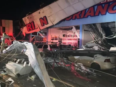 Imagem da passagem do ciclone provocou danos em lojas e carros parados na rua, com diversos destroços na rua e um poste caído em cima de um carro branco