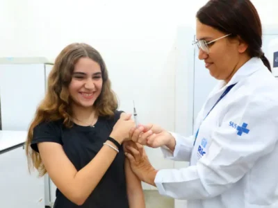 Adolescente recebe vacina de profissional de saúde durante campanha de multivacinação no Rio
