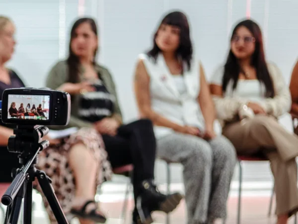 Mulheres participam de atividade audiovisual com câmera em primeiro plano; curso gratuito encerra inscrições em Maricá