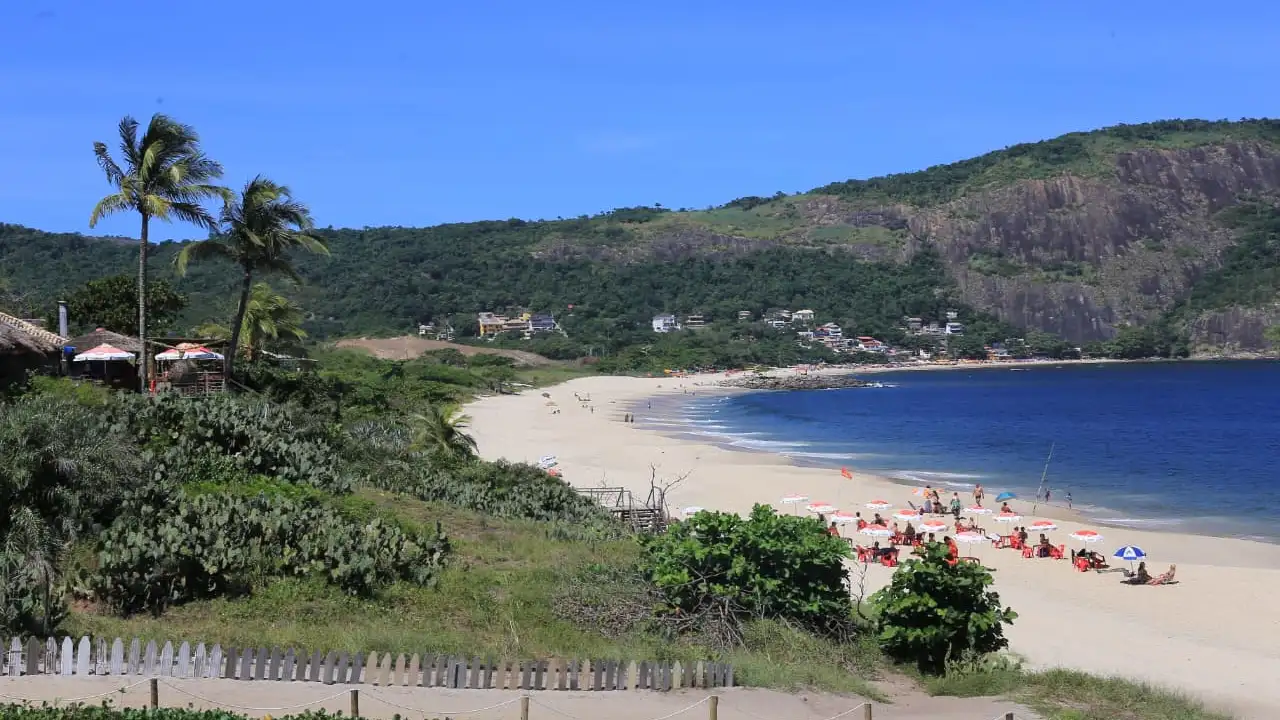 Vista panorâmica de praia de Niterói cercada por vegetação, morros e faixa de areia