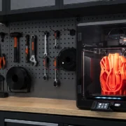 Impressora 3D em bancada maker com peça laranja em impressão