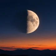 Lua em fase crescente aparece no céu ao entardecer sobre o horizonte de montanhas.