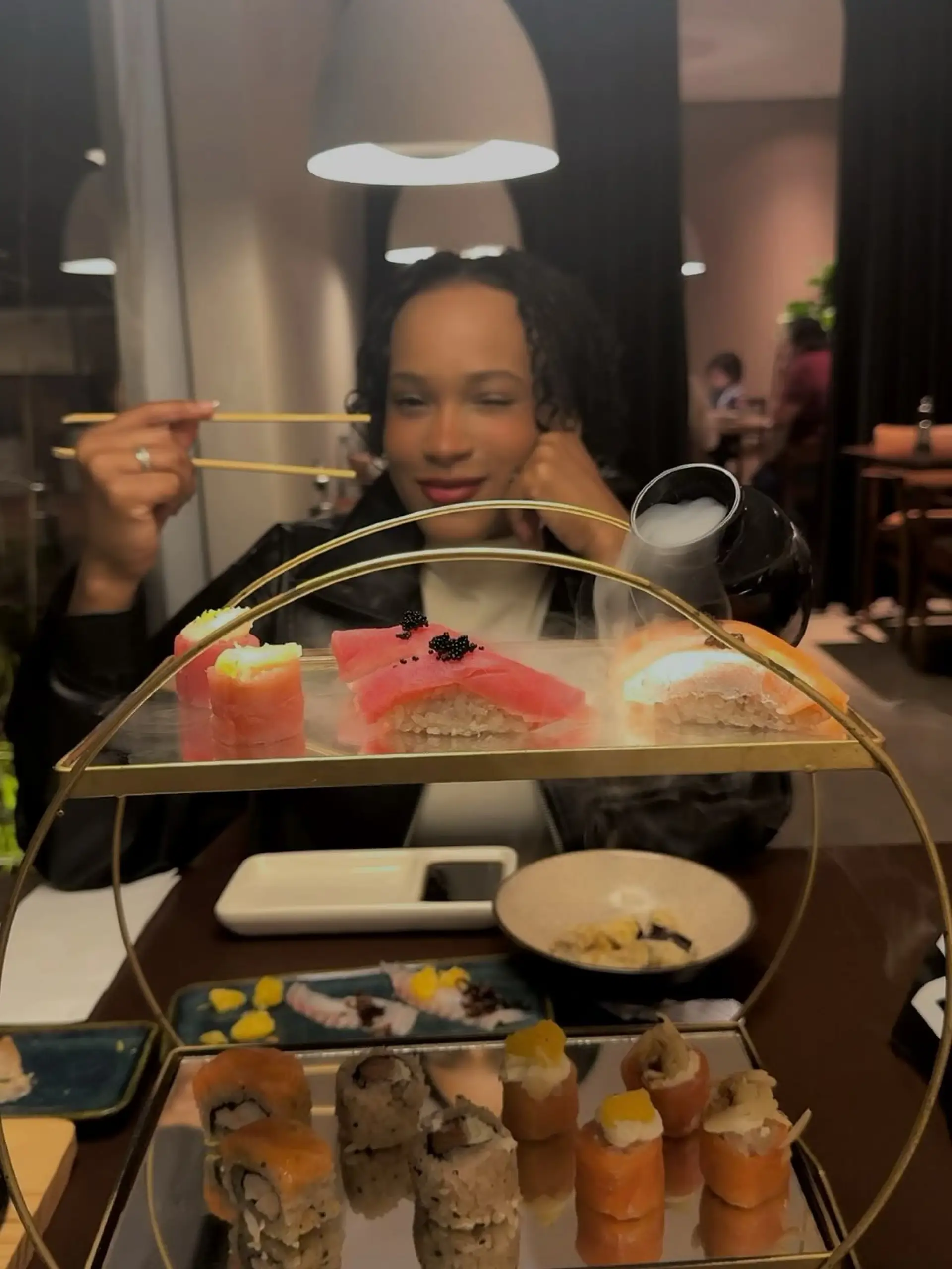 Rebeca Andrade durante refeição em restaurante com pratos de comida japonesa sobre a mesa