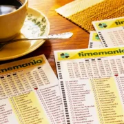 Mesa sobreposta com volantes da lotomania acompanhados de uma xícara com café, pires e colher, para ilustração de reportagem sobre o concurso 2438 da Timemania, com resultado dos números sorteados no domingo, 06/09, bem como prêmios de todas as faixas de acerto. Soma do total de apostas realizadas, e análises econômicas, financeiras e lotéricas tanto sobre as ganhadoras quanto perdedoras, com base na arrecadação.