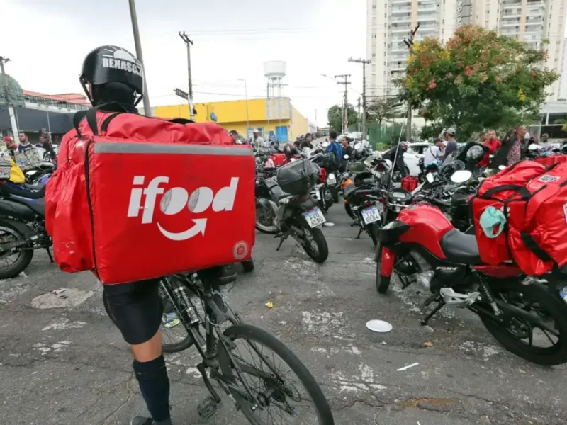Entregador de aplicativo com bicicleta e mochila do iFood entre motociclistas em área urbana