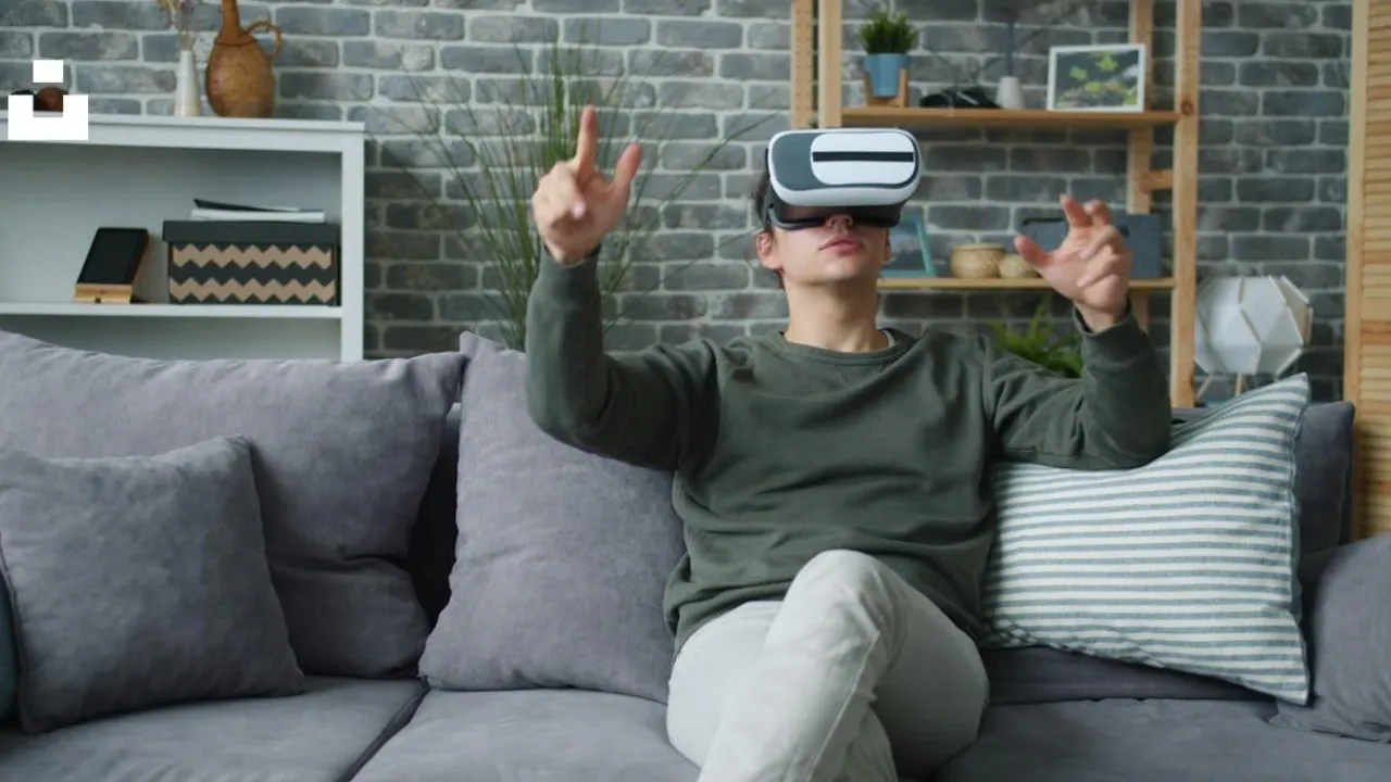 Homem sentado no sofá utiliza óculos de realidade virtual e movimenta as mãos durante uma experiência VR. Homem sentado no sofá utiliza óculos de realidade virtual e movimenta as mãos durante uma experiência VR.