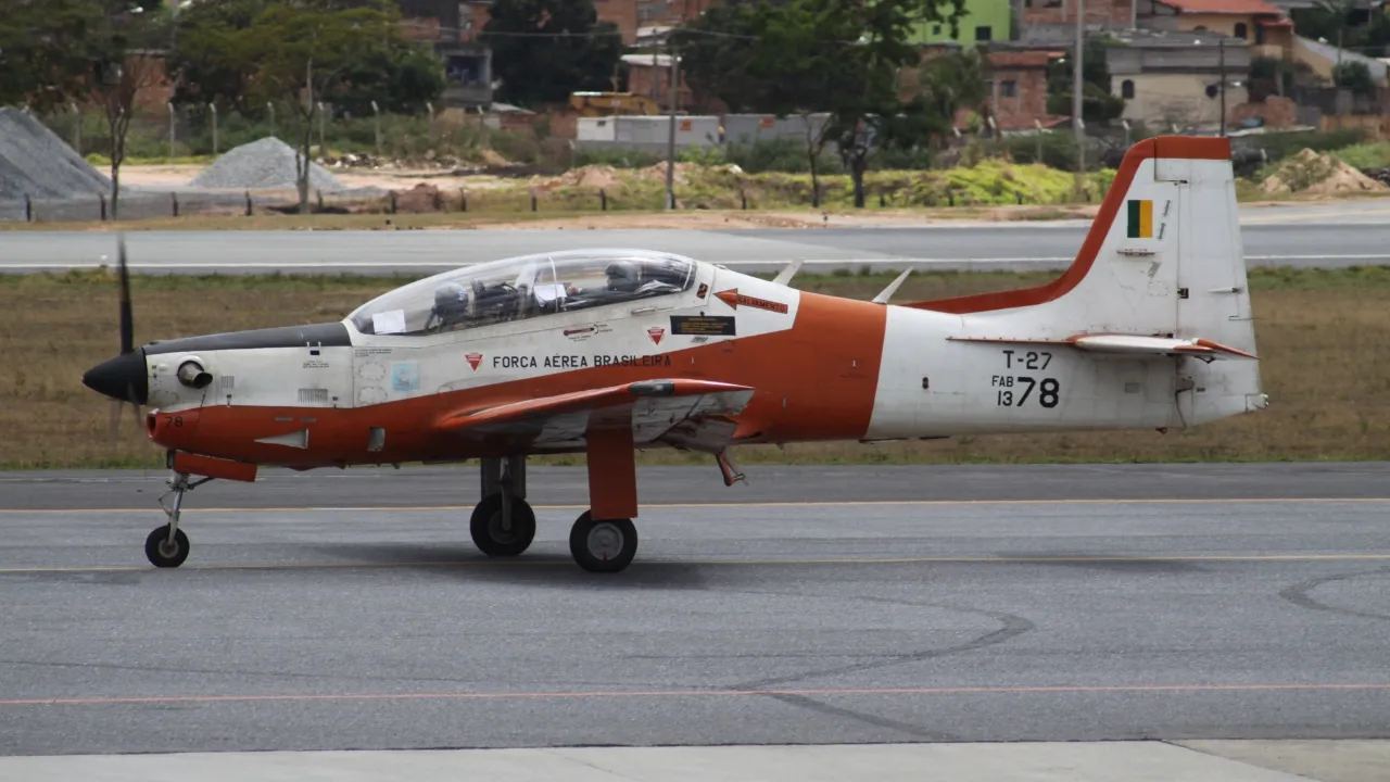 Avião militar Embraer T-27 Tucano da Força Aérea Brasileira em solo, com pintura branca e laranja.