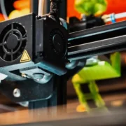 Cabeçote de impressora 3D em close, mostrando ventilador de refrigeração, componentes do extrusor e estrutura metálica.
