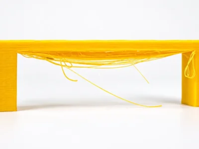 Peça de teste de impressão 3D com linhas de filamento suspensas entre dois pilares, demonstrando a técnica de bridging.