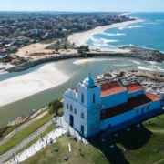 Vista aérea da Igreja de Nossa Senhora de Nazareth, em Saquarema, com praias, lagoa e o Oceano Atlântico ao fundo.