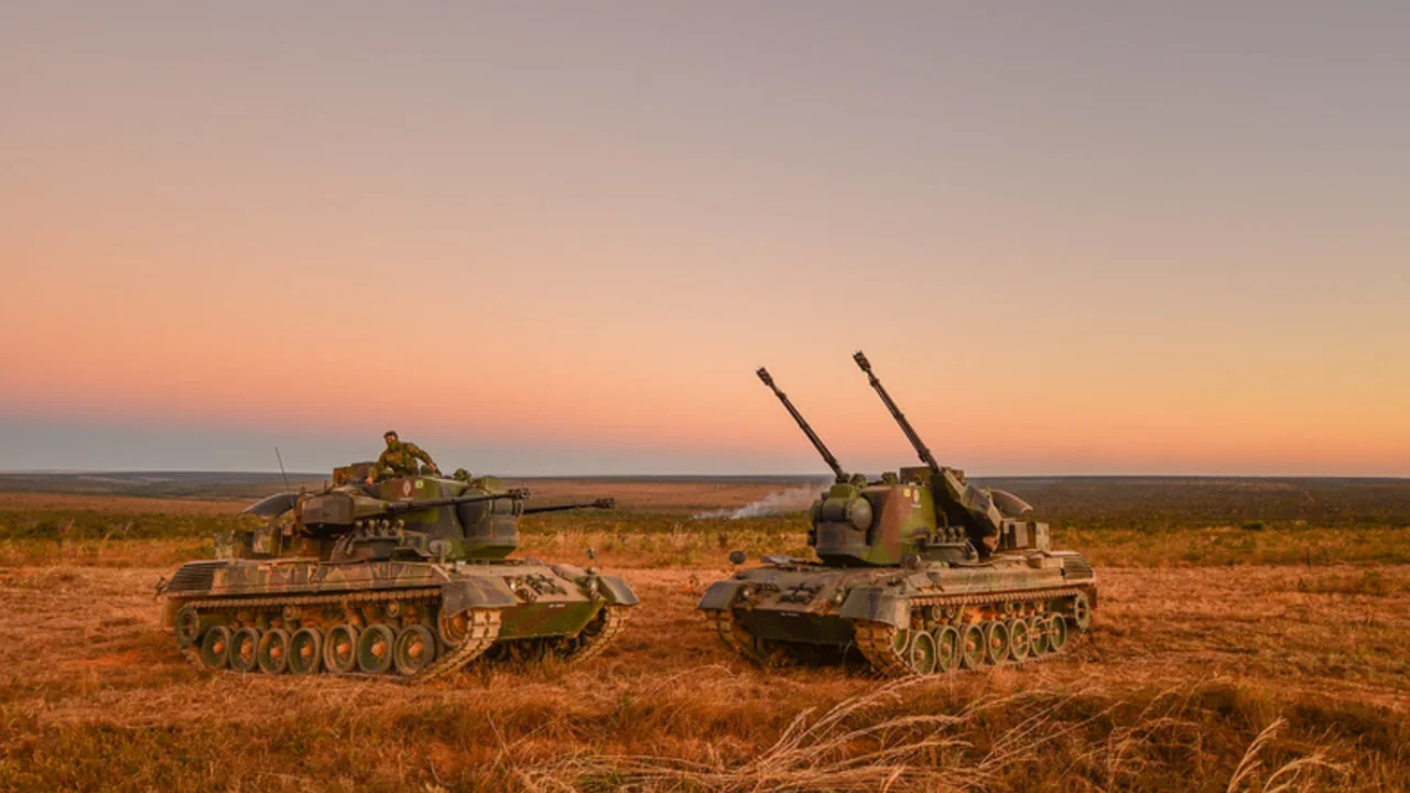 Dois veículos blindados de artilharia antiaérea com canhões elevados, posicionados em campo aberto ao entardecer.