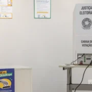 Urna eletrônica instalada em cabine de votação da Justiça Eleitoral, ao lado de compartimento para guardar celulares.
