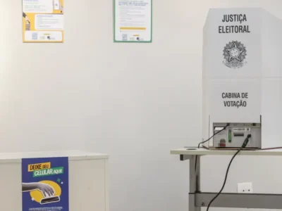 Urna eletrônica instalada em cabine de votação da Justiça Eleitoral, ao lado de compartimento para guardar celulares.