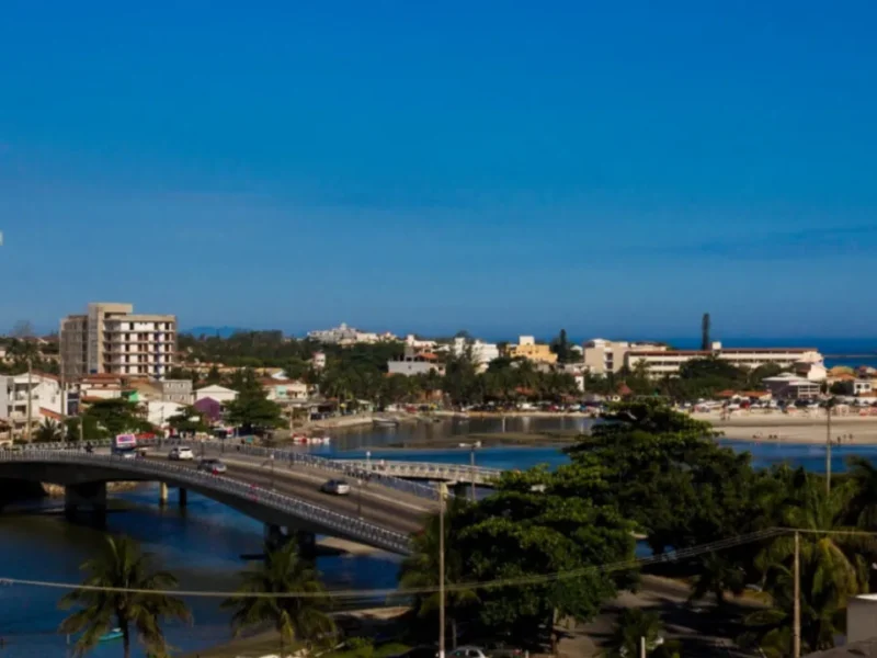 Vista panorâmica de Saquarema, com ponte sobre a lagoa, área urbana, vegetação e praia ao fundo.