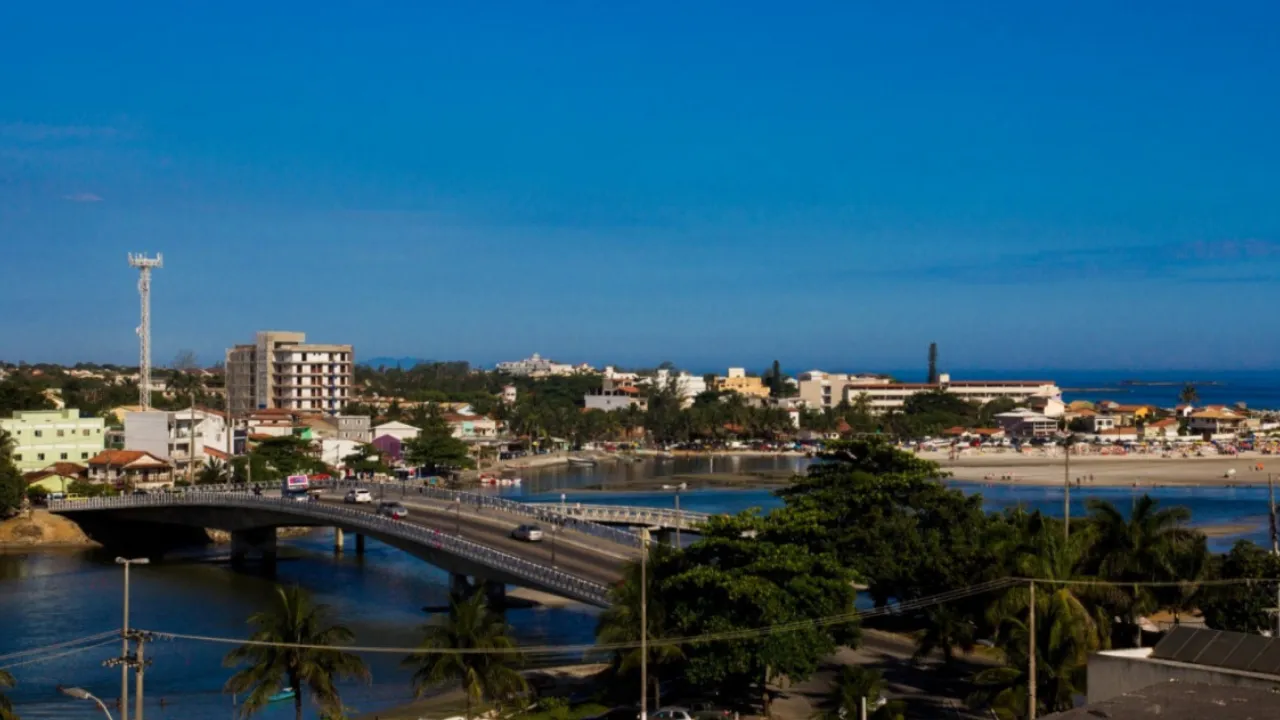 Vista panorâmica de Saquarema, com ponte sobre a lagoa, área urbana, vegetação e praia ao fundo.