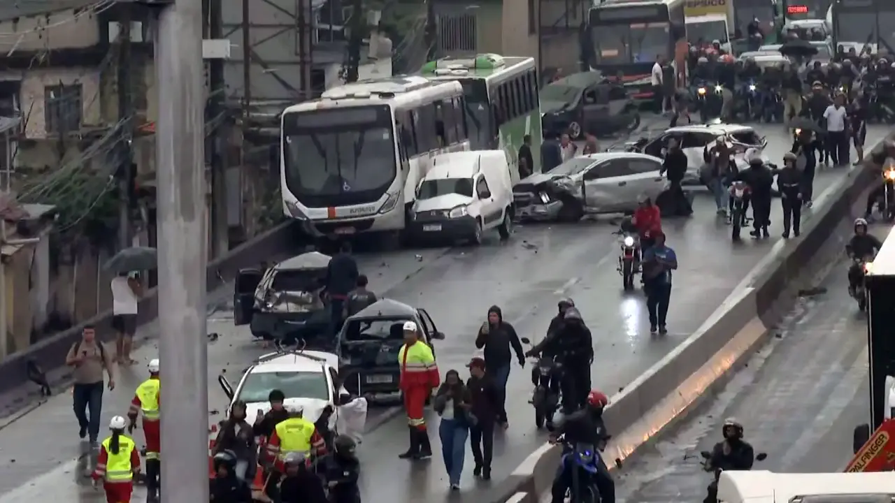 Vista geral do engavetamento na Via Dutra mostra ônibus, carros destruídos, equipes de resgate e pessoas caminhando entre os veículos acidentados.