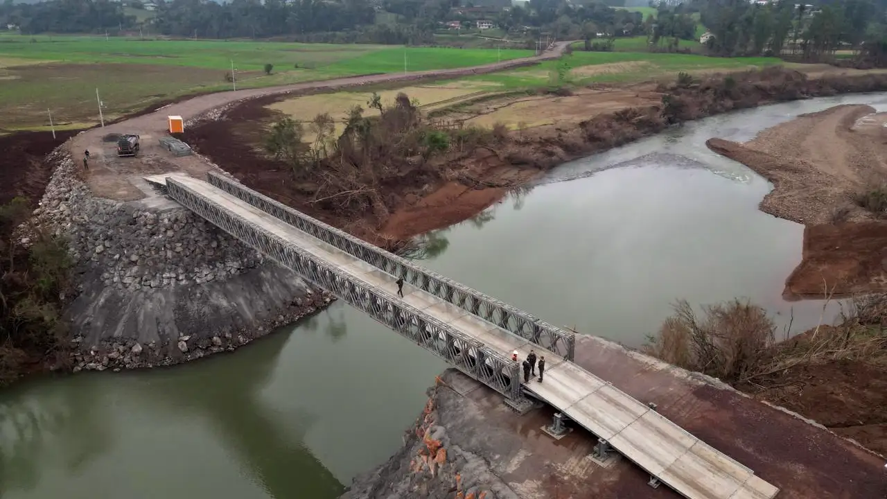 Vista aérea de ponte metálica modular instalada sobre um rio, conectando duas margens em área rural. Vista aérea de ponte metálica modular instalada sobre um rio, conectando duas margens em área rural.