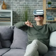 Homem sentado no sofá utiliza óculos de realidade virtual, ilustrando reportagem sobre enjoo em jogos VR e ajustes de conforto.
