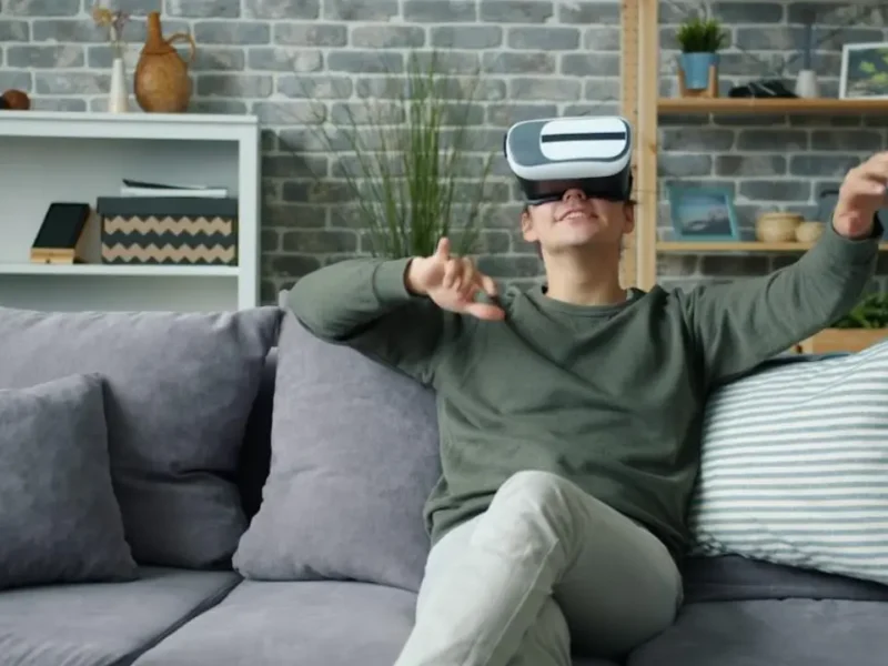 Homem sentado no sofá utiliza óculos de realidade virtual, ilustrando reportagem sobre enjoo em jogos VR e ajustes de conforto.