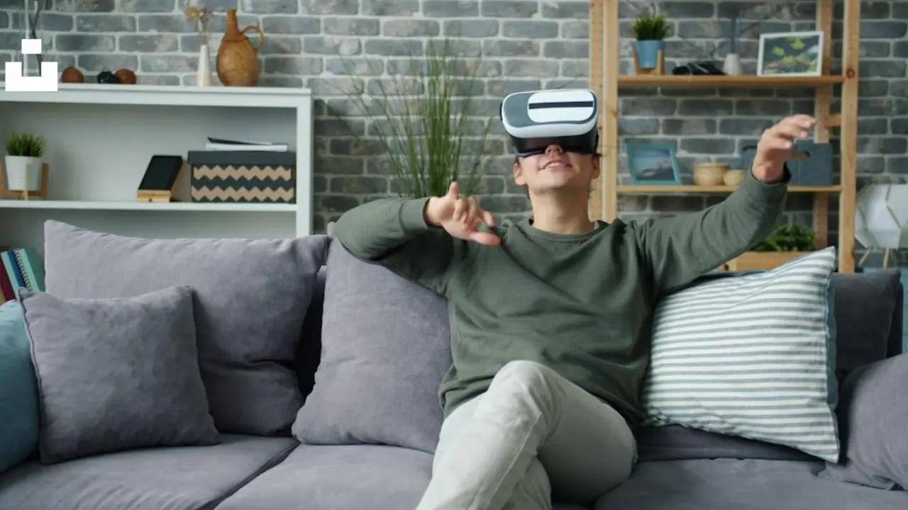 Homem sentado no sofá utiliza óculos de realidade virtual, ilustrando reportagem sobre enjoo em jogos VR e ajustes de conforto. Homem sentado no sofá utiliza óculos de realidade virtual, ilustrando reportagem sobre enjoo em jogos VR e ajustes de conforto.