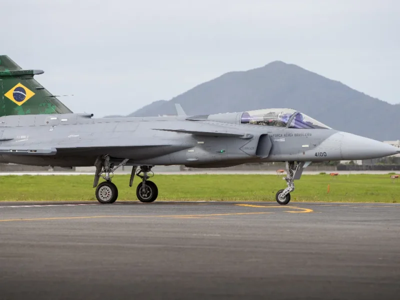 Caça F-39 Gripen de matrícula militar 4100 da Força Aérea Brasileira em uma pista, visto de perfil.