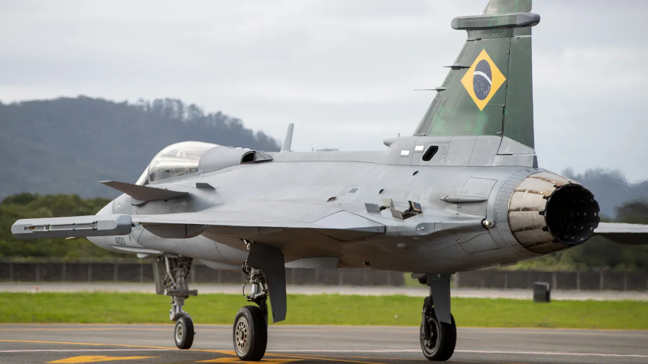 Caça F-39 Gripen da Força Aérea Brasileira visto pela traseira, com motor, asas e bandeira do Brasil na cauda.