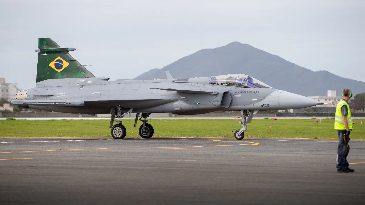 Caça F-39 Gripen de matrícula militar 4100 da Força Aérea Brasileira em uma pista, visto de perfil.