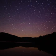 Céu estrelado refletido em lago entre montanhas durante a noite
