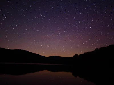 Céu estrelado refletido em lago entre montanhas durante a noite