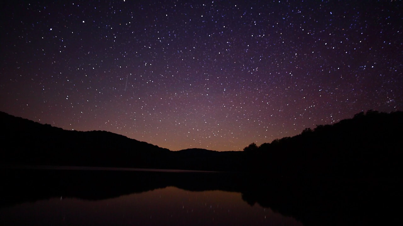 Céu estrelado refletido em lago entre montanhas durante a noite