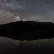 Via Láctea sobre montanha com reflexo em lago durante a noite