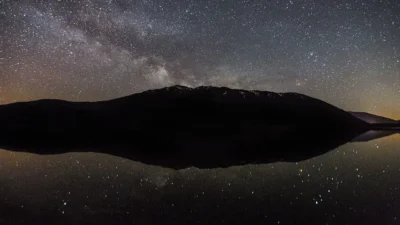 Via Láctea sobre montanha com reflexo em lago durante a noite